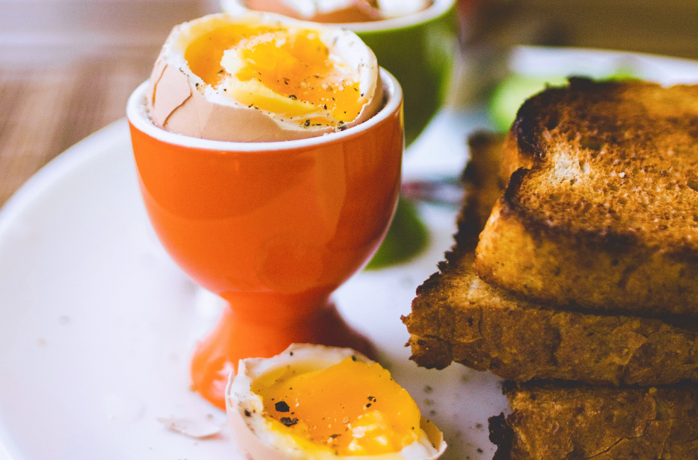 jammy eggs in a holder next to a stack of toast to show a post on two ways to get the perfect jammy eggs