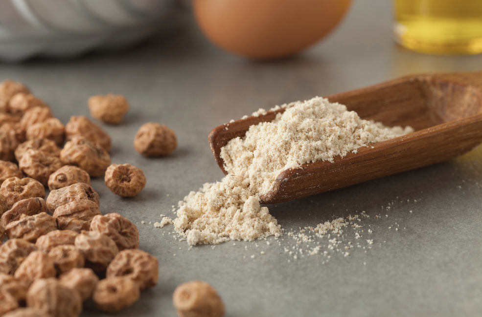 A pile of whole tiger nuts on the left with a wooden scoop of ground tiger nut flour on the right as the image for article titles tiger nut are a versatile ingredient.